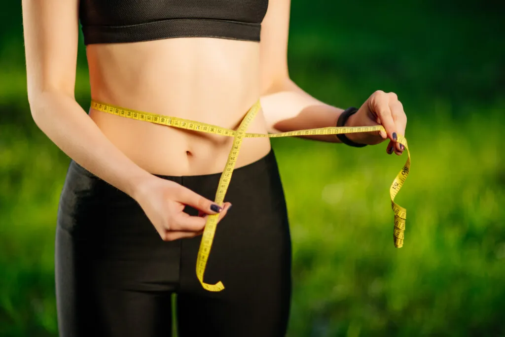 young woman measuring her thin waist with tape measure 1