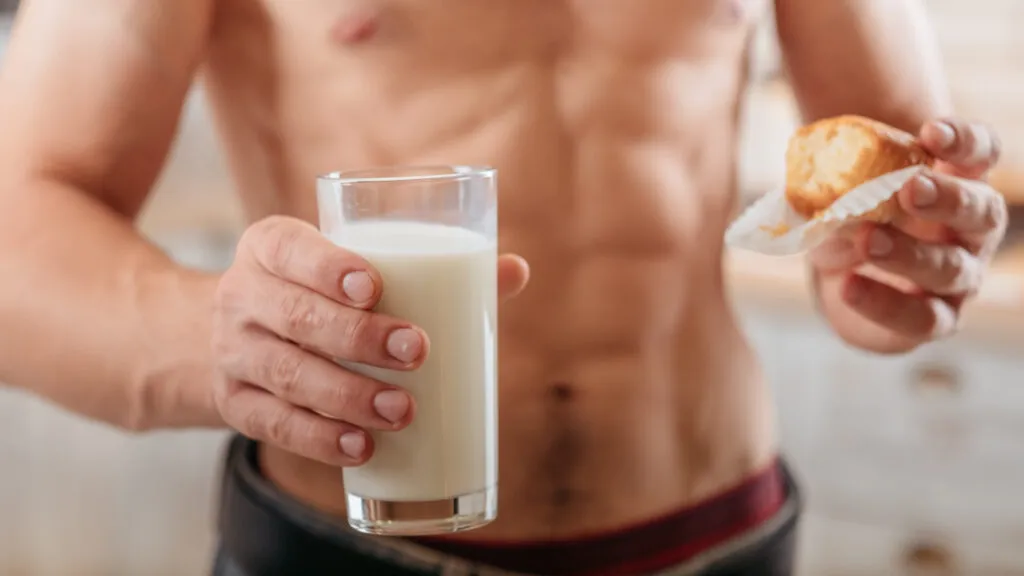 sport nutrition cropped shot man with bare torso eating muffin with soy milk