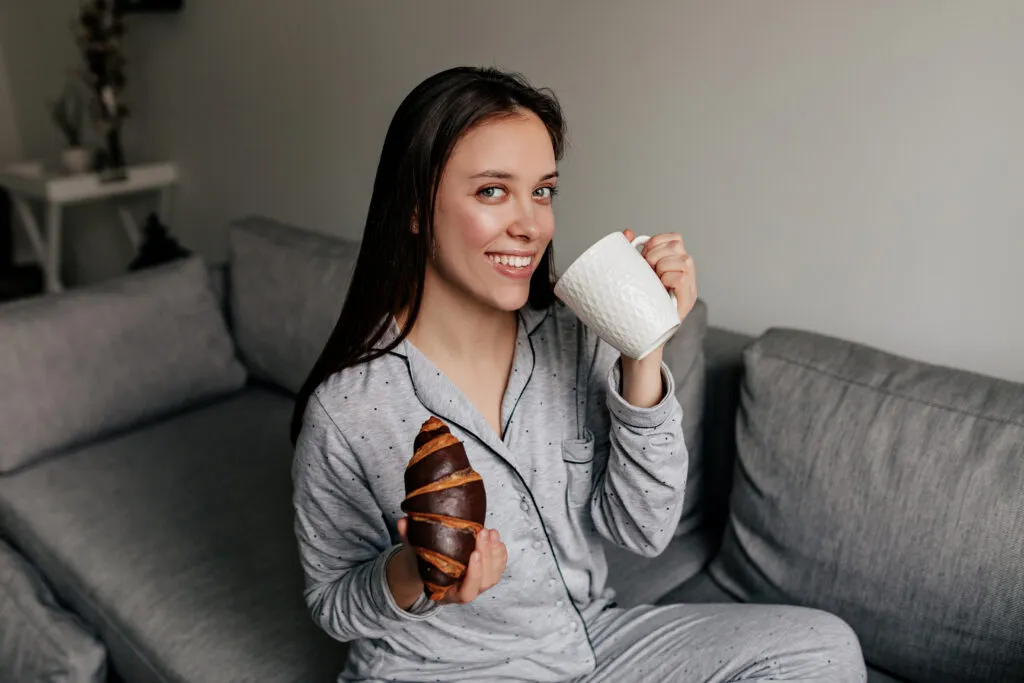 attractive lovely woman with wonderful smile wearing pajamas drinking coffee eating croissants home good sunny day
