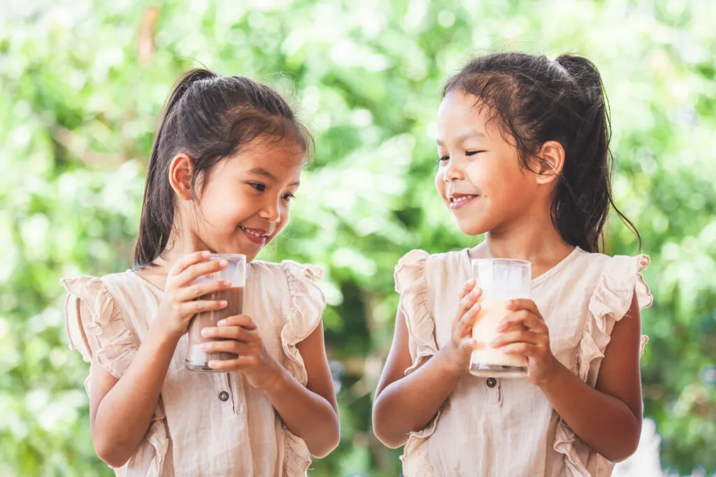 two cute asian child girls drinking milk from glass together