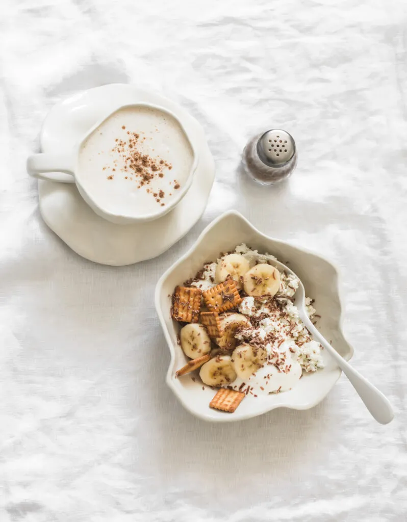 delicious breakfast brunch cottage cheese with banana sour cream crackers chocolate cappuccino light background top view