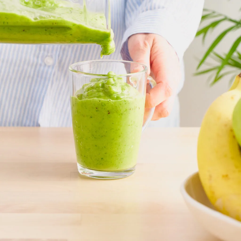 raw foodism green smoothie with banana spinach woman pouring detox drink from blender