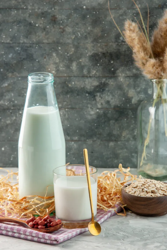 vertical view open glass bottle cup filled with milk bean spoon purple stripped towel